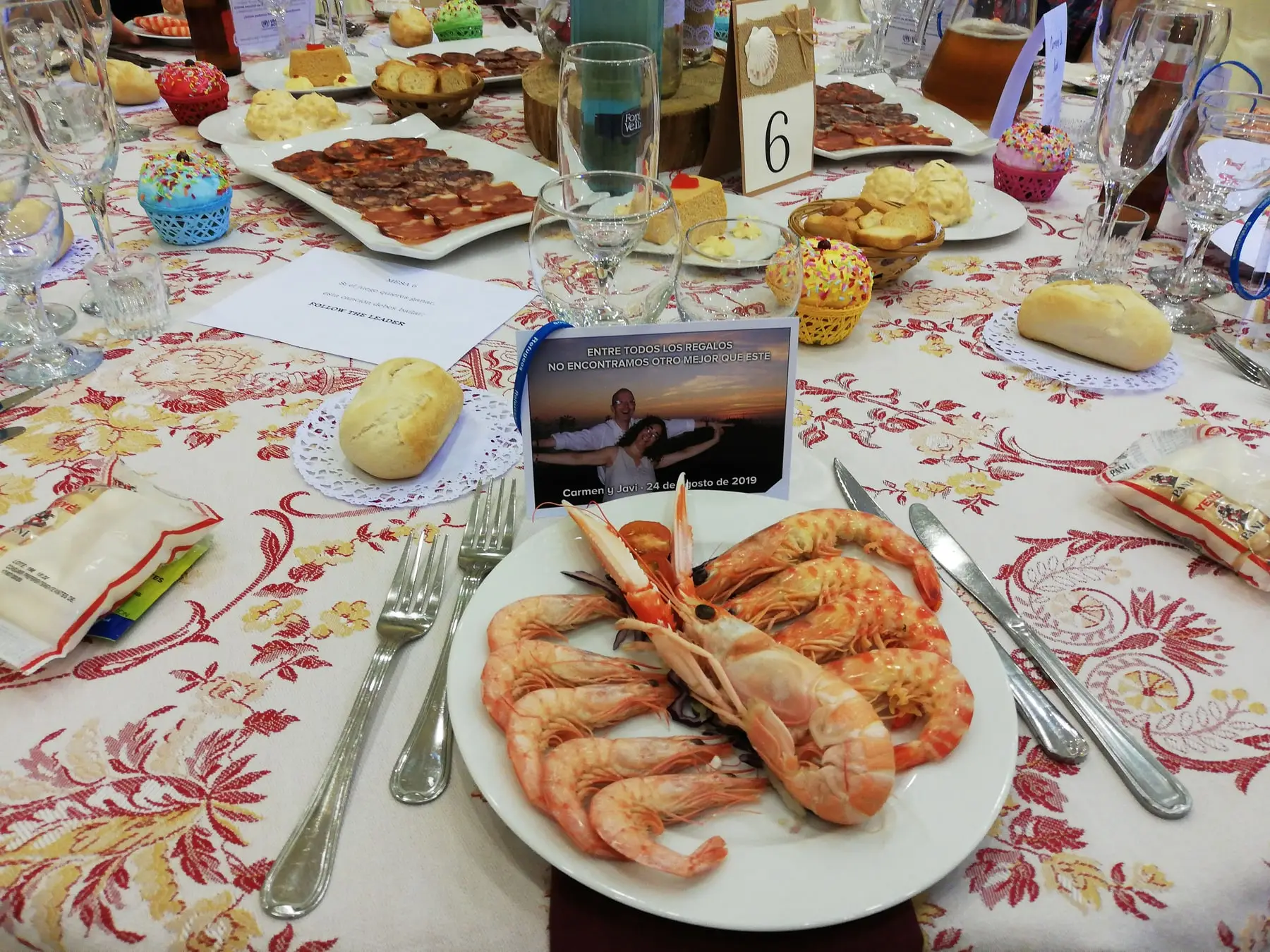 Un plato de langostinos sobre un mantel de flores rojas y un minutero con foto de los novios