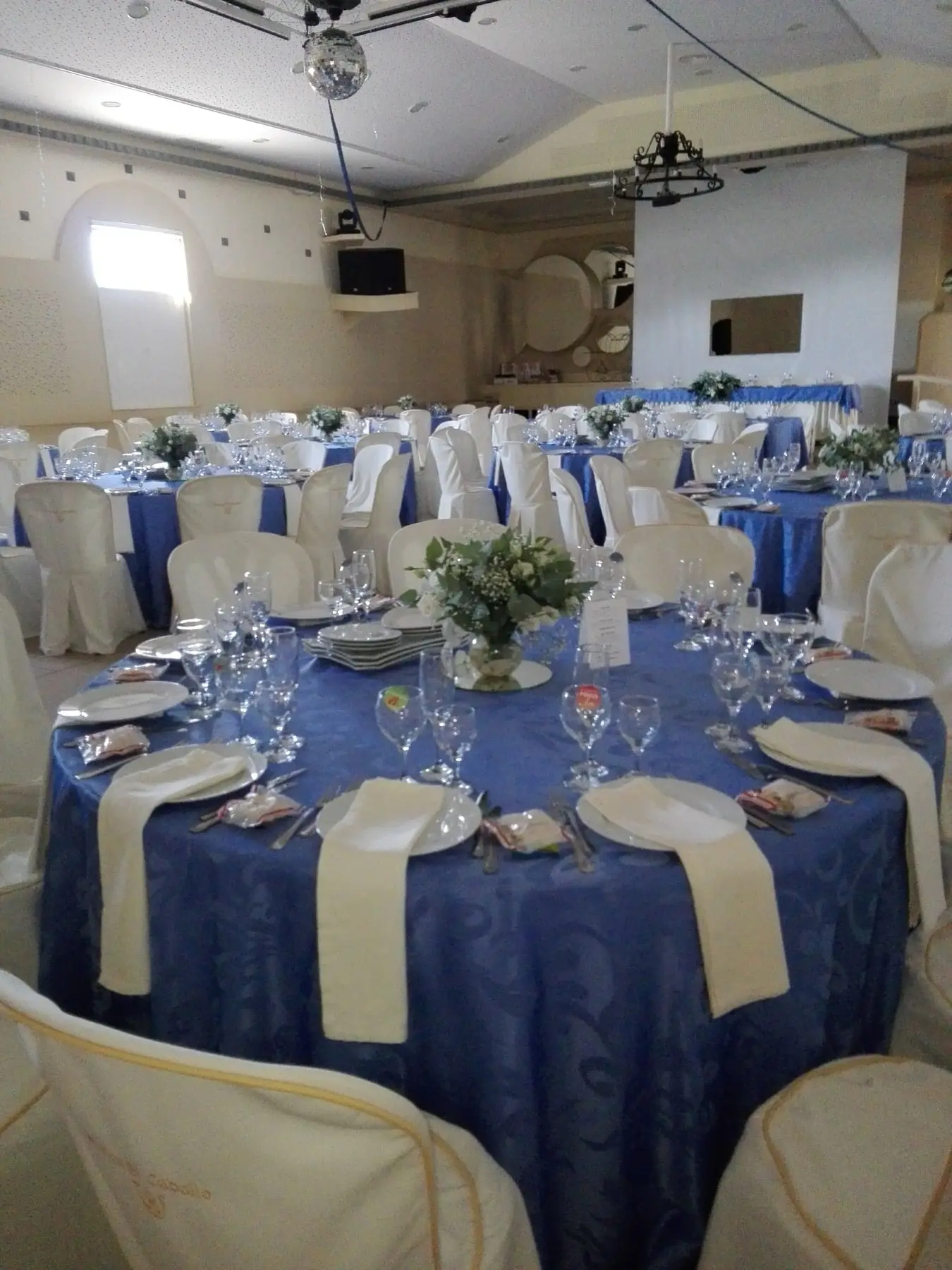 El salón con mesas redondas vestidas de azul, sillas con funda blanca y una bola de espejos
